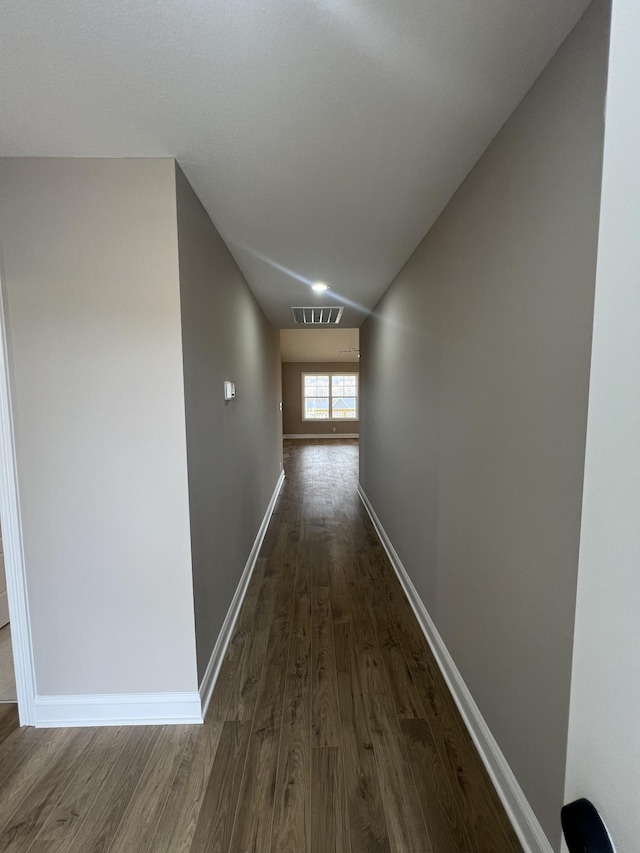 hallway featuring visible vents, dark wood finished floors, and baseboards