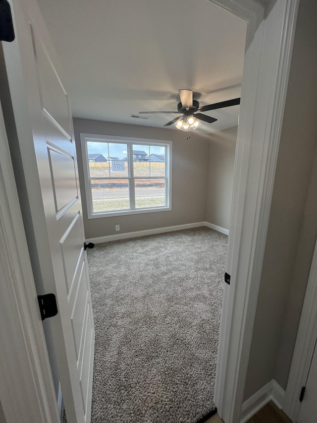 empty room featuring a ceiling fan, baseboards, visible vents, and carpet flooring