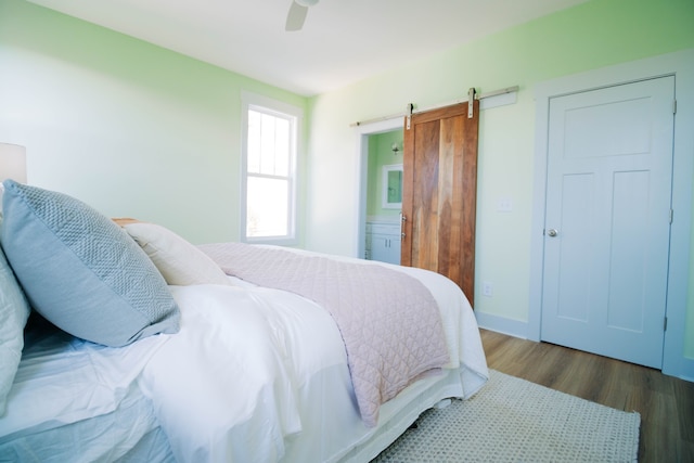 bedroom featuring ensuite bath, dark wood-type flooring, a barn door, and ceiling fan