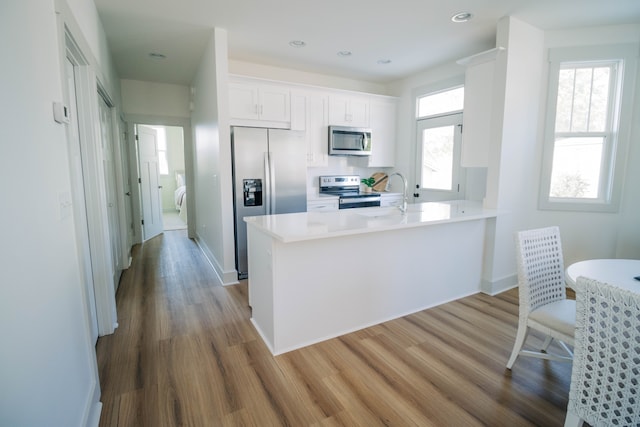 kitchen featuring hardwood / wood-style flooring, kitchen peninsula, stainless steel appliances, sink, and white cabinets