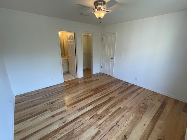 unfurnished bedroom featuring a closet, ensuite bathroom, light wood-type flooring, and ceiling fan