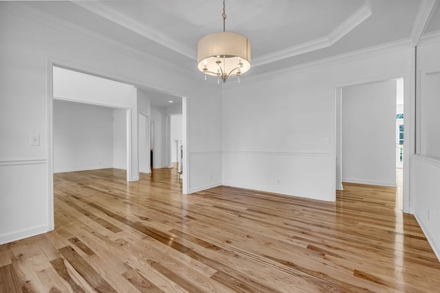 unfurnished dining area featuring a raised ceiling, ornamental molding, light hardwood / wood-style flooring, and an inviting chandelier