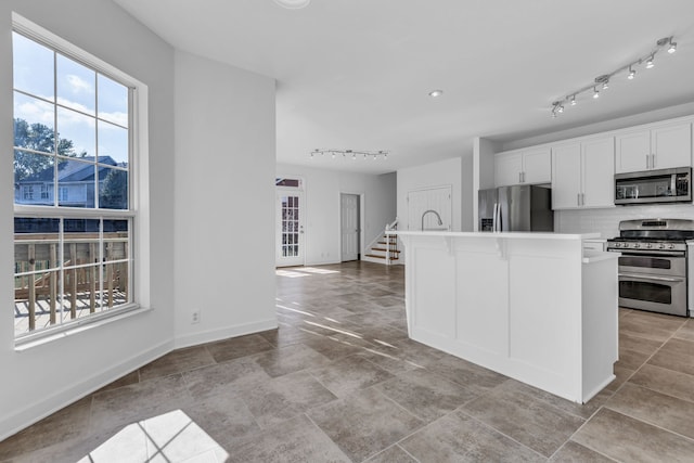 kitchen featuring stainless steel appliances, backsplash, a center island, rail lighting, and white cabinets