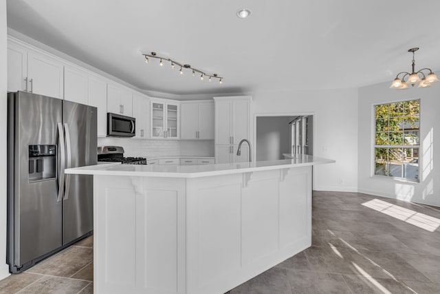 kitchen with white cabinets, appliances with stainless steel finishes, pendant lighting, and a kitchen island with sink