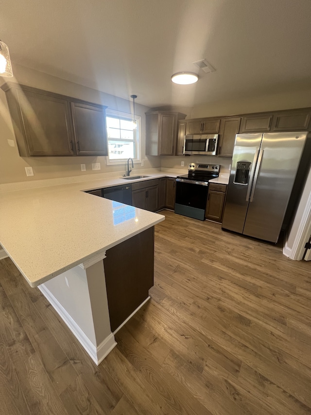 kitchen with kitchen peninsula, appliances with stainless steel finishes, dark wood-type flooring, sink, and pendant lighting