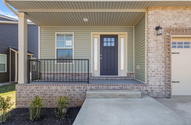 view of exterior entry with a garage, a porch, and brick siding