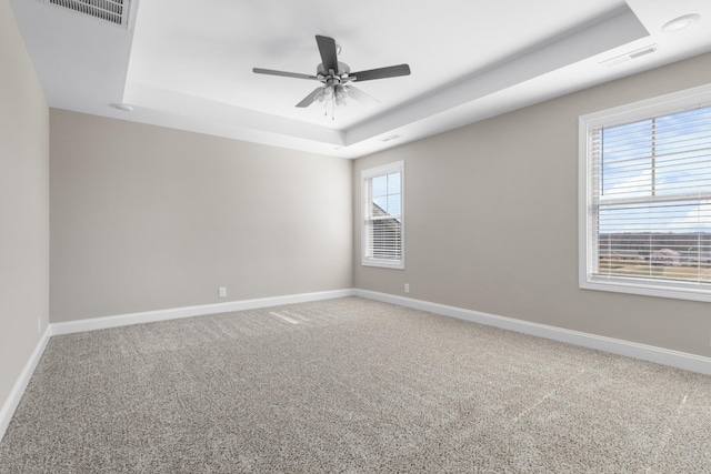 unfurnished room featuring a tray ceiling, carpet, and visible vents