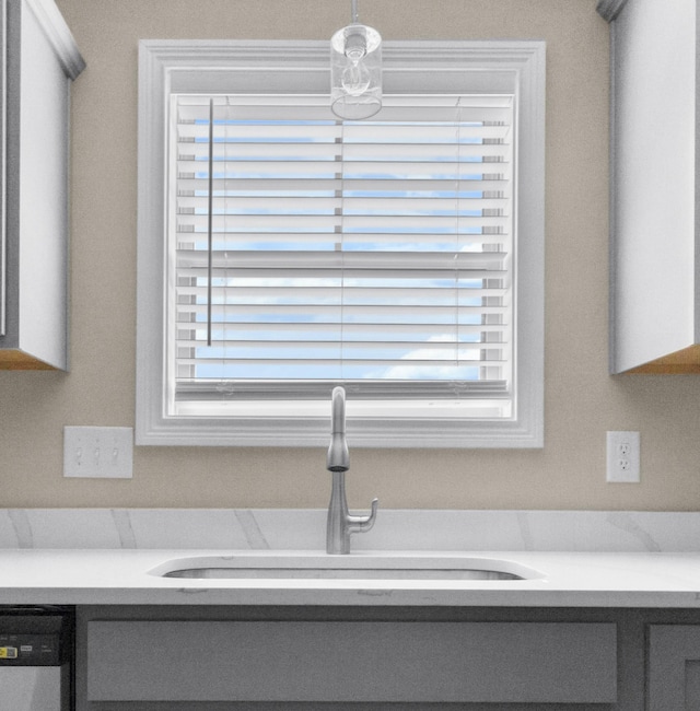 interior details featuring stainless steel dishwasher, light countertops, a sink, and gray cabinetry