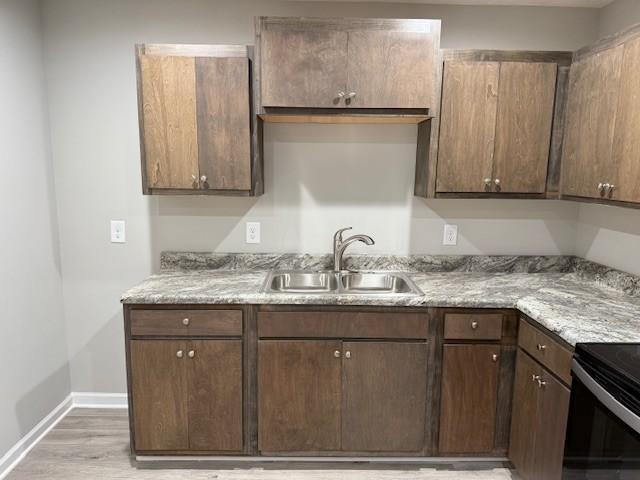 kitchen with dark brown cabinets, sink, light stone counters, and light hardwood / wood-style flooring