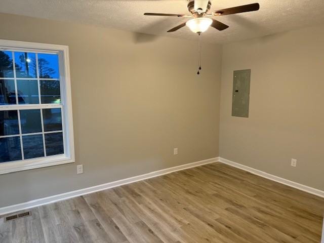 spare room featuring ceiling fan, wood-type flooring, electric panel, and a textured ceiling