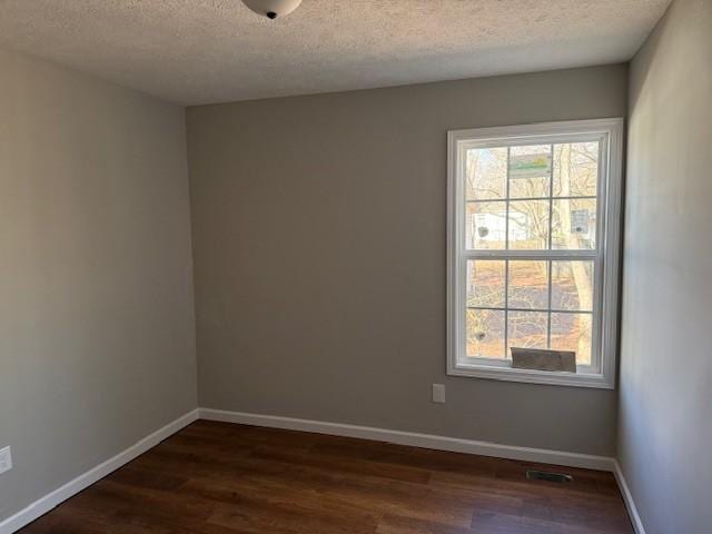 empty room with plenty of natural light, dark hardwood / wood-style flooring, and a textured ceiling