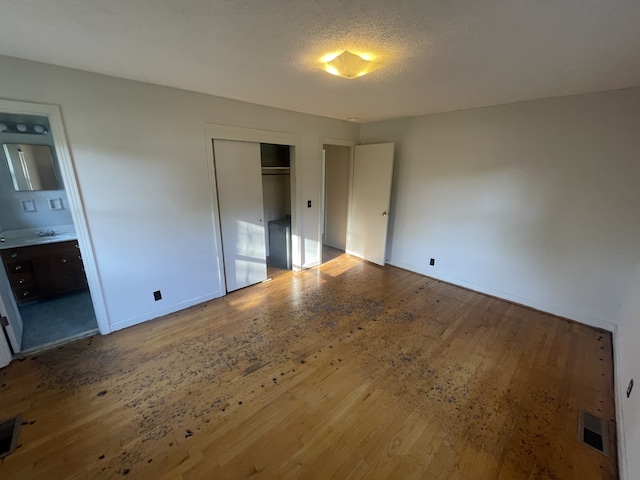 unfurnished bedroom featuring a closet, ensuite bath, a textured ceiling, and hardwood / wood-style floors