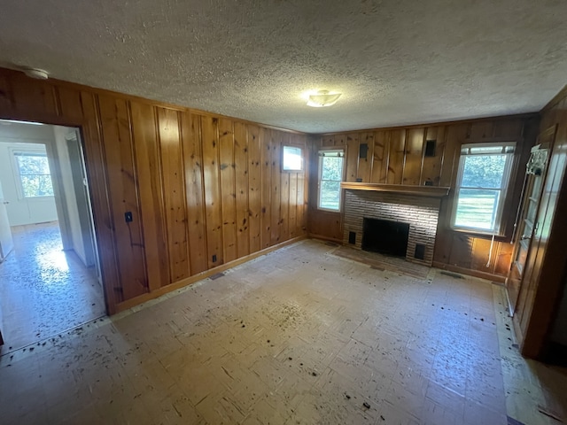 unfurnished living room featuring a brick fireplace, a textured ceiling, and wood walls