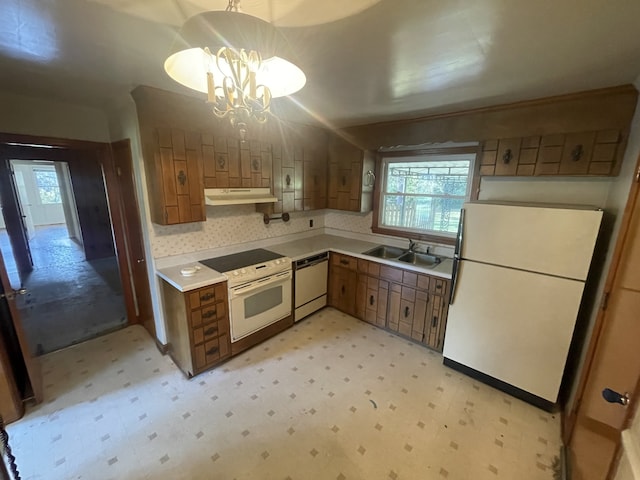 kitchen with white appliances, pendant lighting, sink, and a chandelier