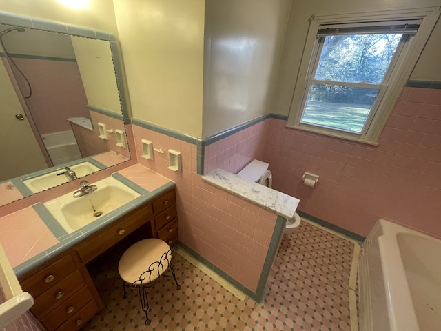 bathroom with vanity, toilet, a tub to relax in, and tile walls