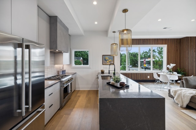 kitchen with a healthy amount of sunlight, sink, dark stone counters, high end appliances, and a center island with sink