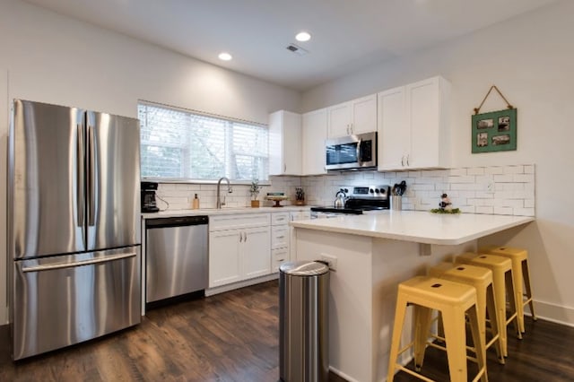 kitchen with dark wood-type flooring, backsplash, a breakfast bar, white cabinetry, and appliances with stainless steel finishes