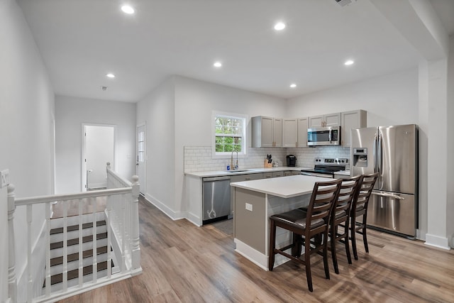 kitchen with appliances with stainless steel finishes, sink, light wood-type flooring, a center island, and gray cabinets