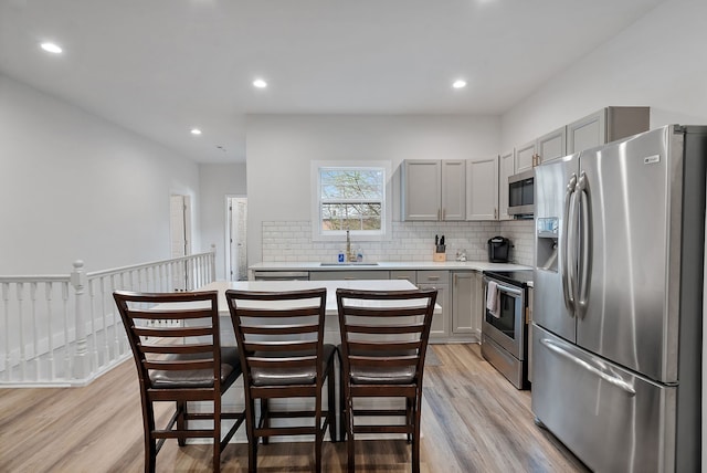 kitchen featuring gray cabinetry, backsplash, sink, light wood-type flooring, and appliances with stainless steel finishes