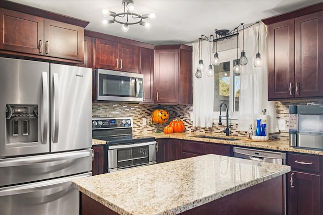 kitchen with light stone counters, backsplash, appliances with stainless steel finishes, sink, and decorative light fixtures