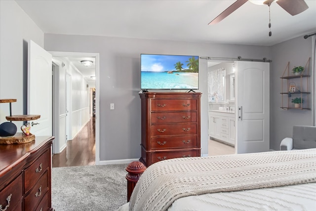 bedroom with ensuite bath, a barn door, light colored carpet, and ceiling fan