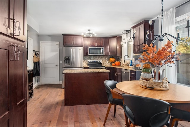 kitchen featuring light stone countertops, appliances with stainless steel finishes, a kitchen island, pendant lighting, and light hardwood / wood-style flooring