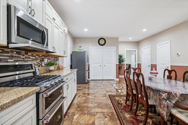 kitchen with light stone counters, stainless steel appliances, backsplash, and white cabinets