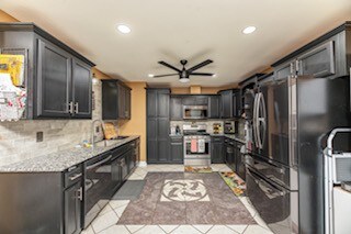 kitchen featuring light stone counters, sink, tasteful backsplash, ceiling fan, and appliances with stainless steel finishes