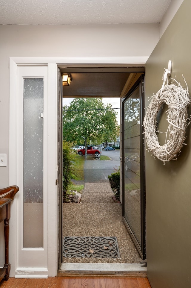 doorway to outside with wood-type flooring, a textured ceiling, and an inviting chandelier