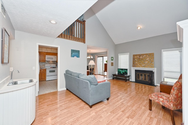 living room with high vaulted ceiling, sink, a textured ceiling, light hardwood / wood-style floors, and a chandelier