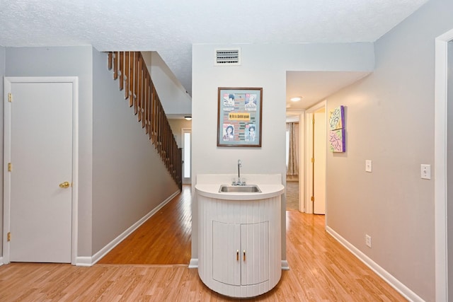 hall featuring sink, light wood-type flooring, and a textured ceiling