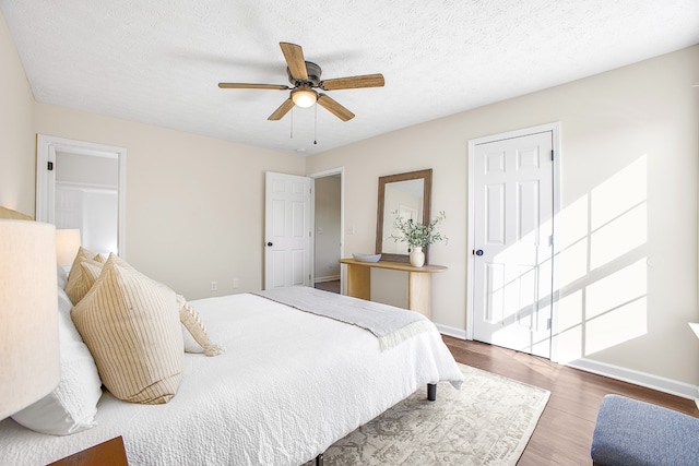 bedroom with a textured ceiling, wood-type flooring, and ceiling fan