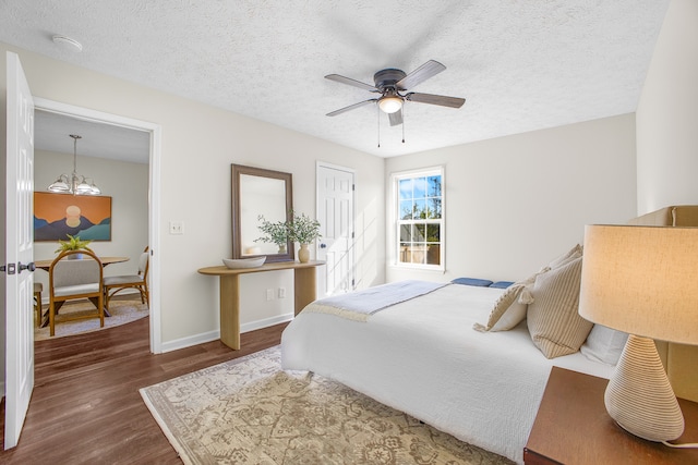 bedroom with a textured ceiling, ceiling fan with notable chandelier, and dark hardwood / wood-style flooring