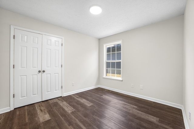 unfurnished bedroom featuring a closet, a textured ceiling, and dark wood-type flooring