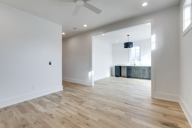 unfurnished living room featuring ceiling fan, sink, and light wood-type flooring