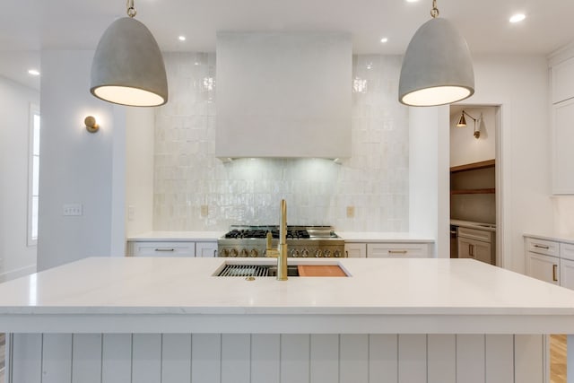 kitchen with decorative backsplash, decorative light fixtures, a center island with sink, light hardwood / wood-style floors, and white cabinetry