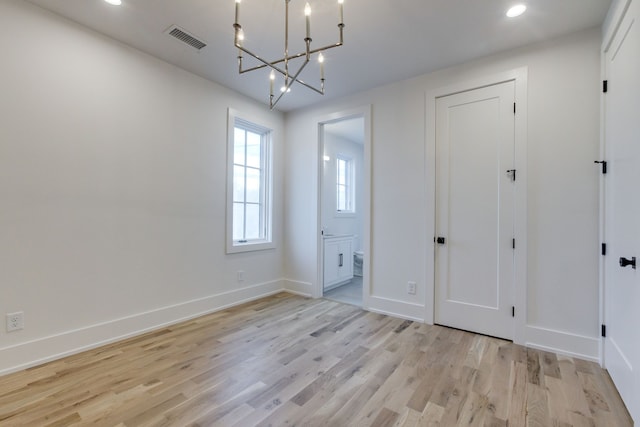 unfurnished bedroom with ensuite bathroom, a notable chandelier, and light wood-type flooring