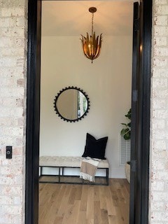 hall with a notable chandelier, wood-type flooring, and brick wall