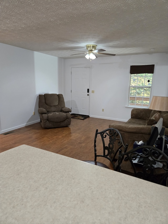 living room with hardwood / wood-style flooring, ceiling fan, and a textured ceiling