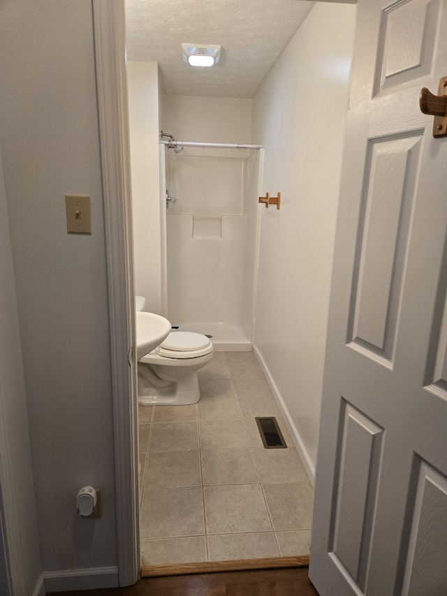 bathroom featuring tile patterned floors, toilet, a shower, and a textured ceiling