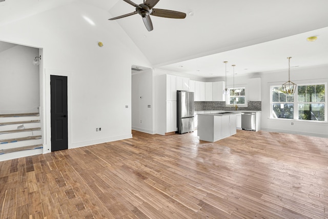 unfurnished living room with sink, ceiling fan with notable chandelier, high vaulted ceiling, and light hardwood / wood-style floors