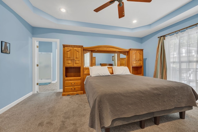 carpeted bedroom featuring a tray ceiling, connected bathroom, and ceiling fan