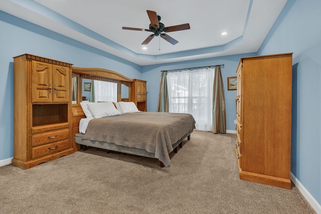 carpeted bedroom with a raised ceiling and ceiling fan