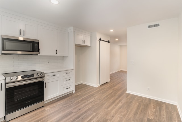 kitchen featuring decorative backsplash, white cabinets, a barn door, light wood-type flooring, and stainless steel appliances