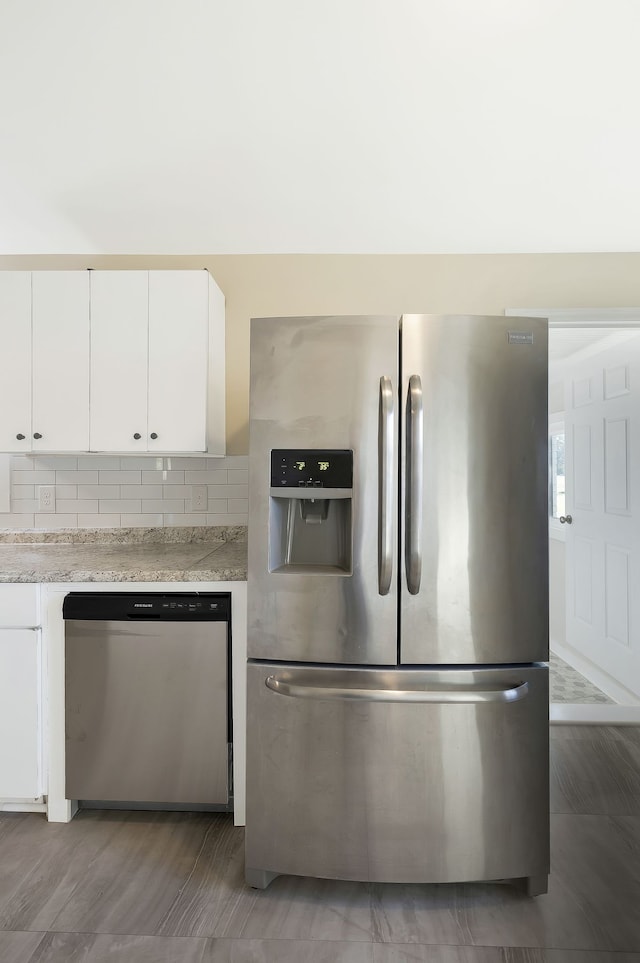 kitchen with light stone countertops, white cabinets, stainless steel appliances, and backsplash