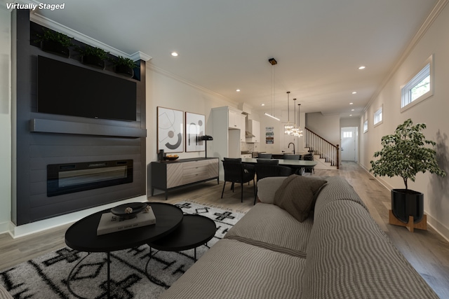 living room with a chandelier, crown molding, and light wood-type flooring