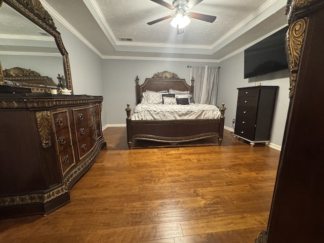 bedroom featuring dark wood-type flooring, a tray ceiling, crown molding, a textured ceiling, and ceiling fan