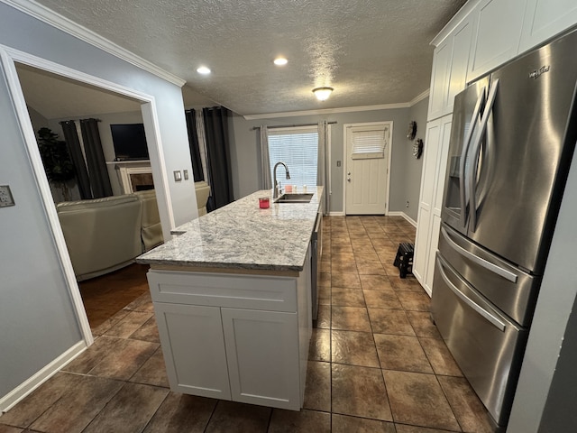 kitchen featuring white cabinets, stainless steel fridge with ice dispenser, a textured ceiling, a kitchen island with sink, and light stone counters