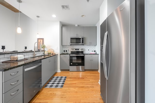 kitchen with appliances with stainless steel finishes, light hardwood / wood-style floors, pendant lighting, and gray cabinetry