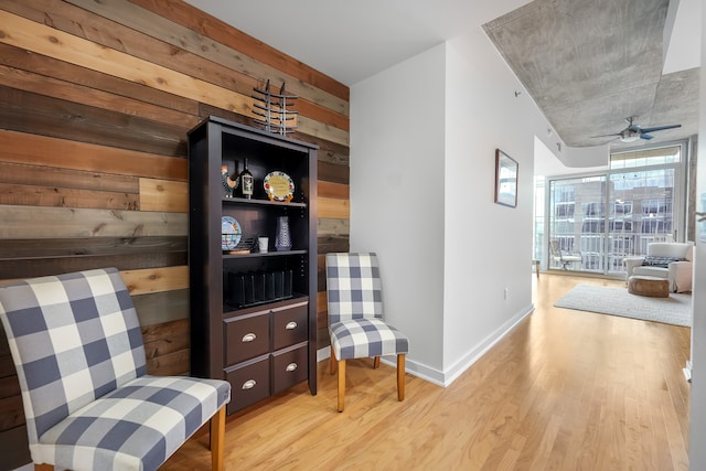 living area with ceiling fan, wooden walls, floor to ceiling windows, and light hardwood / wood-style floors